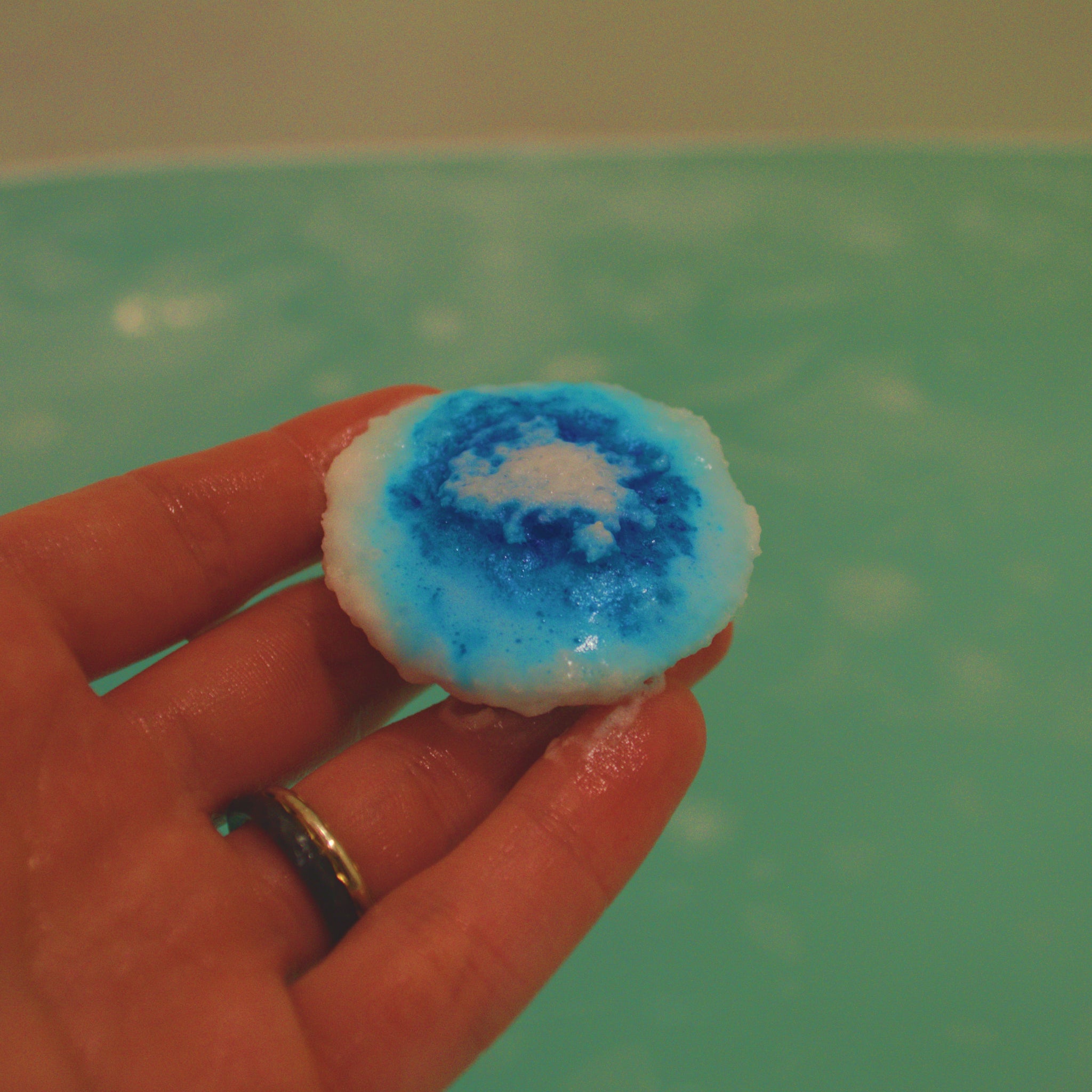Hand holding a blue and white bath bomb against a blue bath background