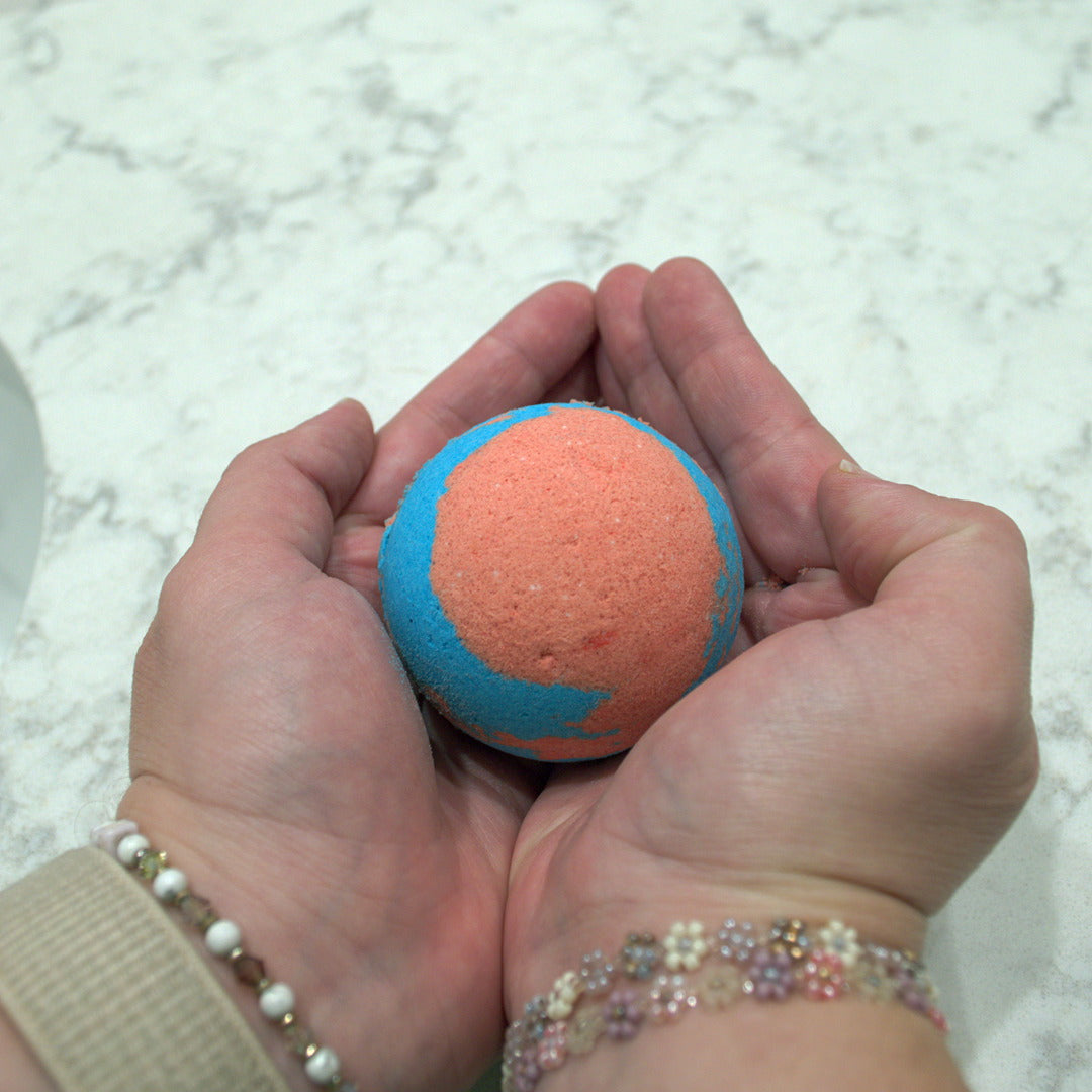 Hand holding a blue and red bath bomb against a white marble background