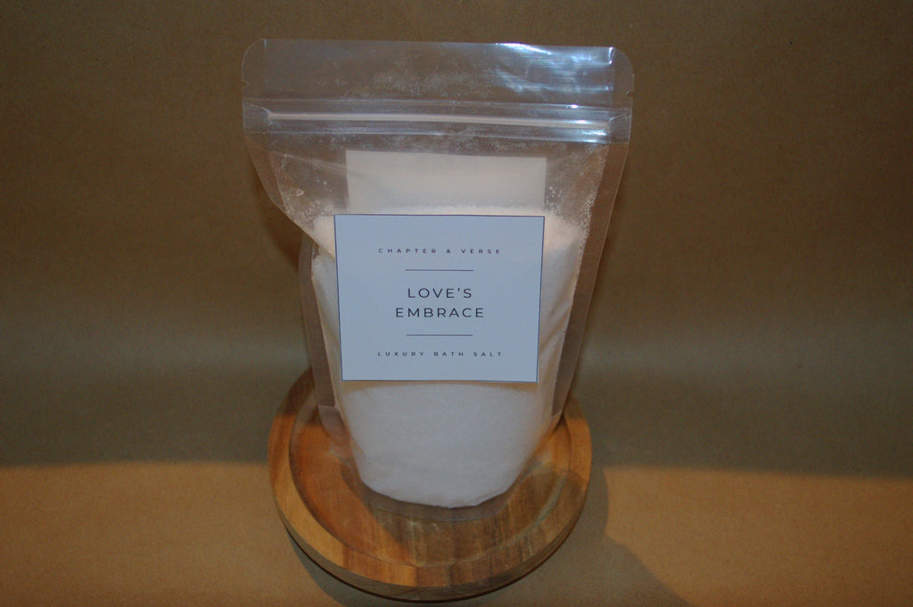 Bag of 'Love's Embrace' bath salts on a wooden stand with a brown background