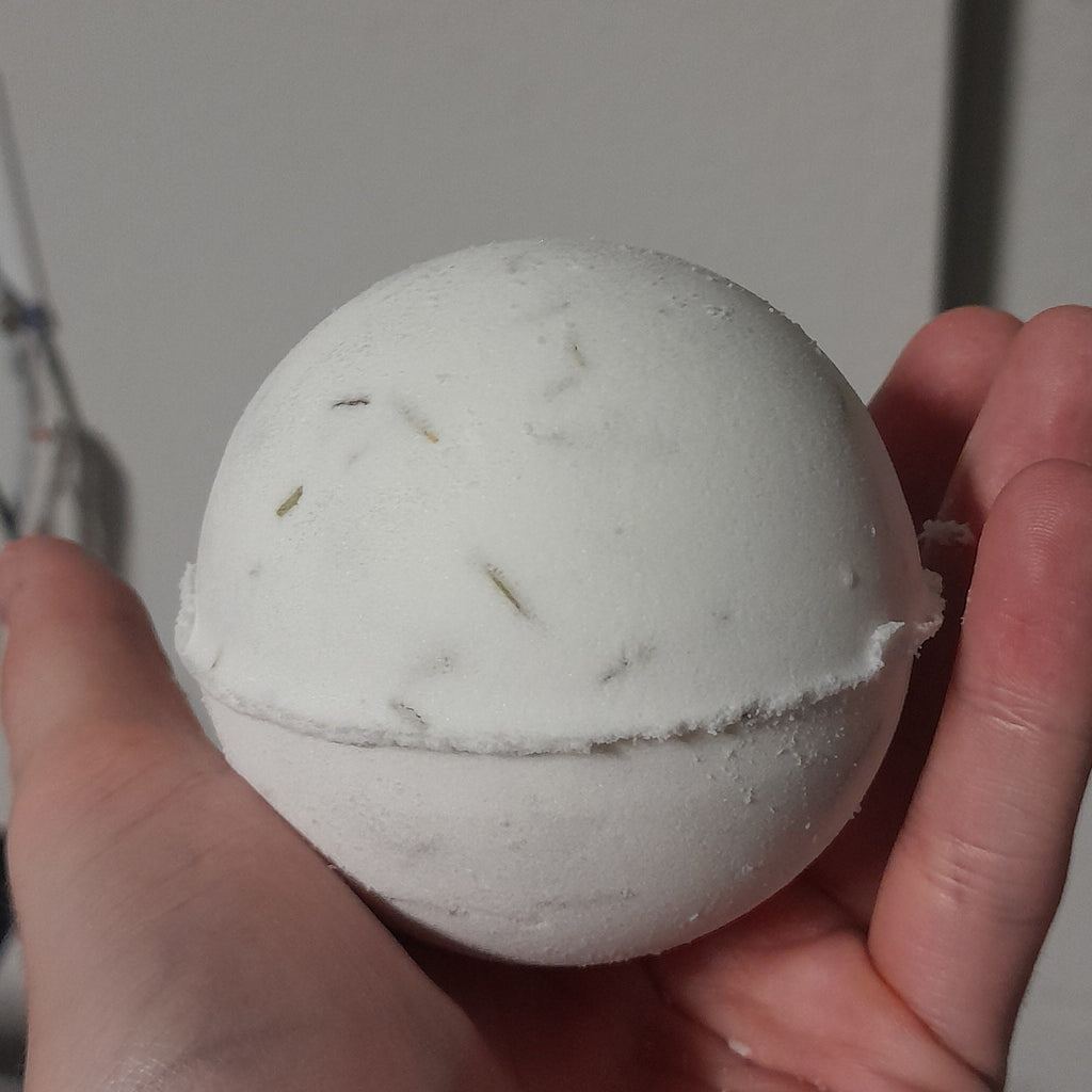 Hand holding a white bath bomb with green specks against a neutral background
