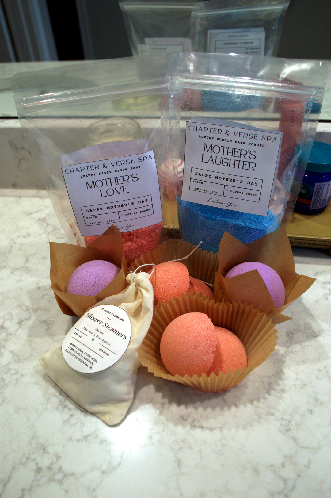 Bath bombs in decorative paper cups with visible labels on a marble surface.