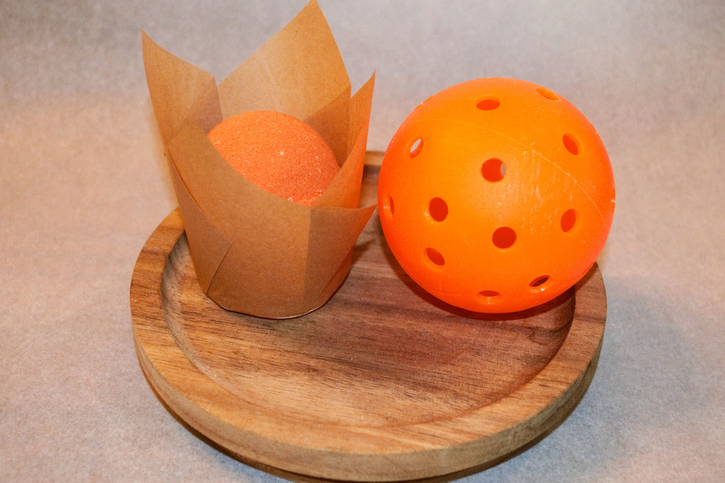 Orange bath bomb size comparison to pickleball
