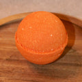Orange bath bomb on a wooden tray with a neutral background