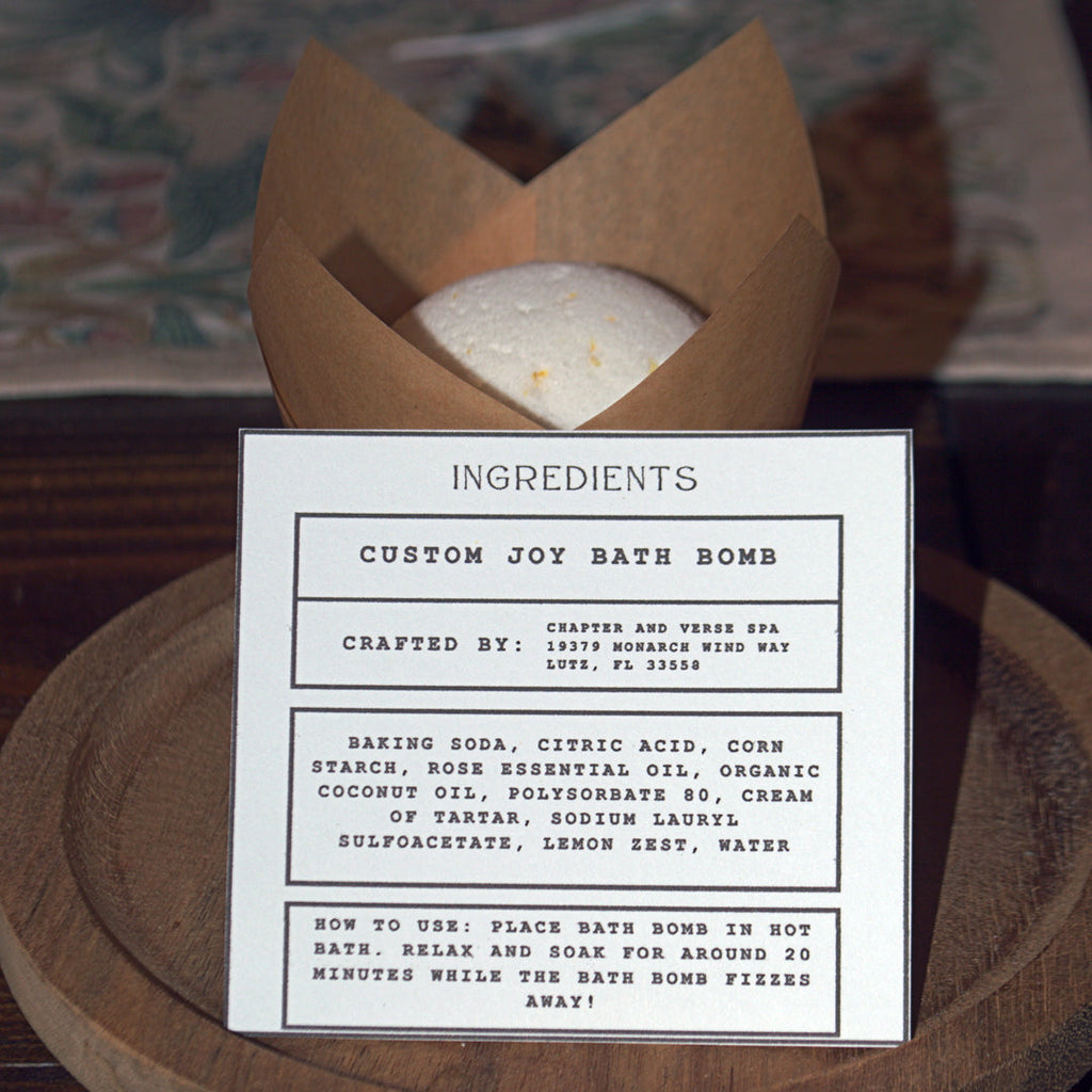 Custom joy bath bomb with ingredients card on a wooden surface