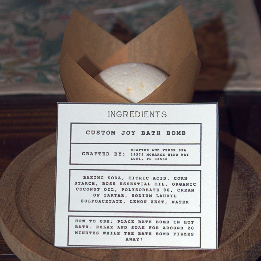 Custom joy bath bomb with ingredients card on a wooden surface