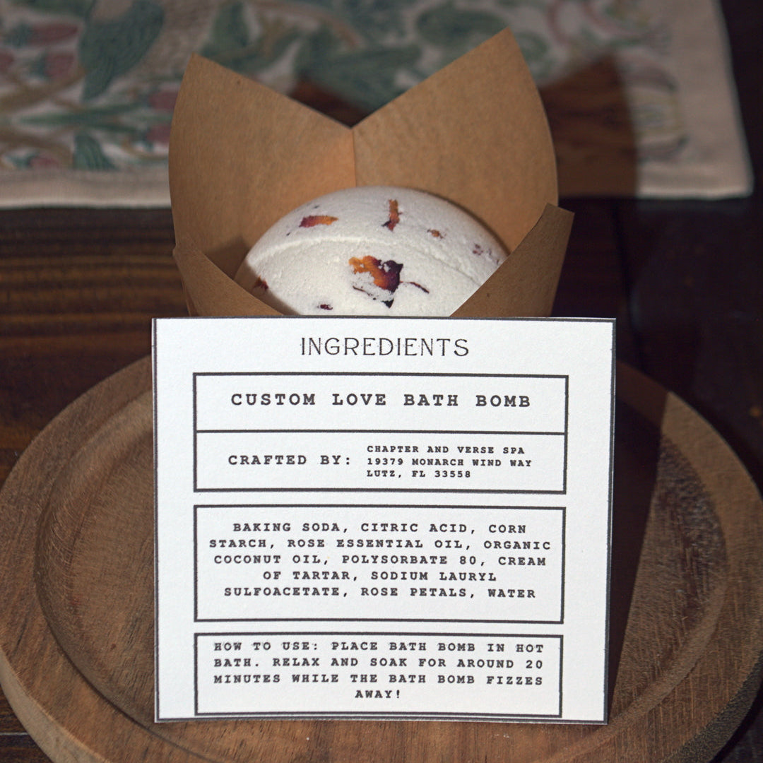 Custom love bath bomb in a brown paper bag with an ingredient label on a wooden surface.