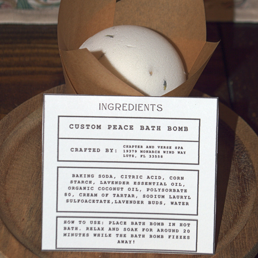 White bath bomb in a brown paper bag with an ingredients label on a wooden surface.