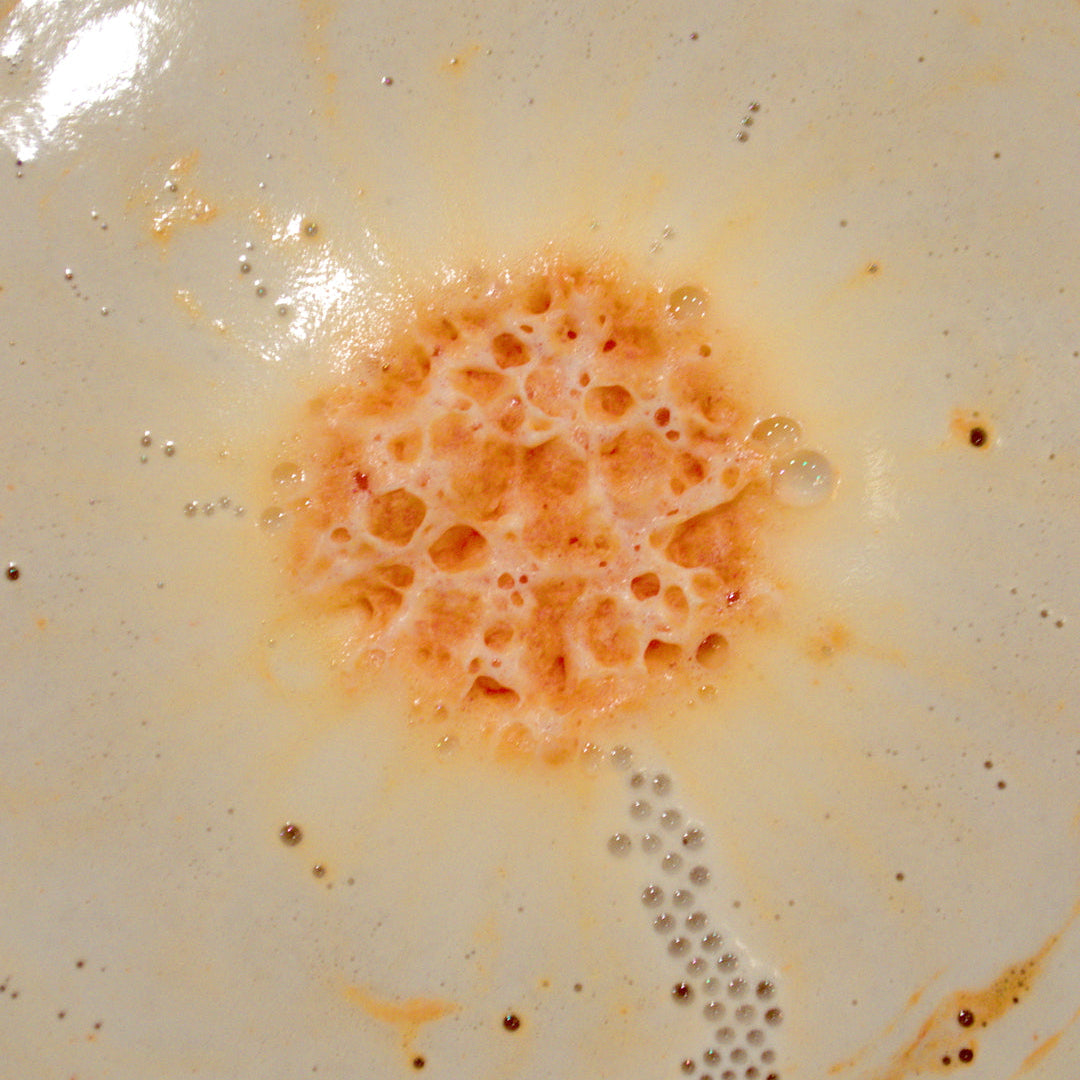 Orange bath bomb dissolving in water surrounded by white and orange foam and bubbles.