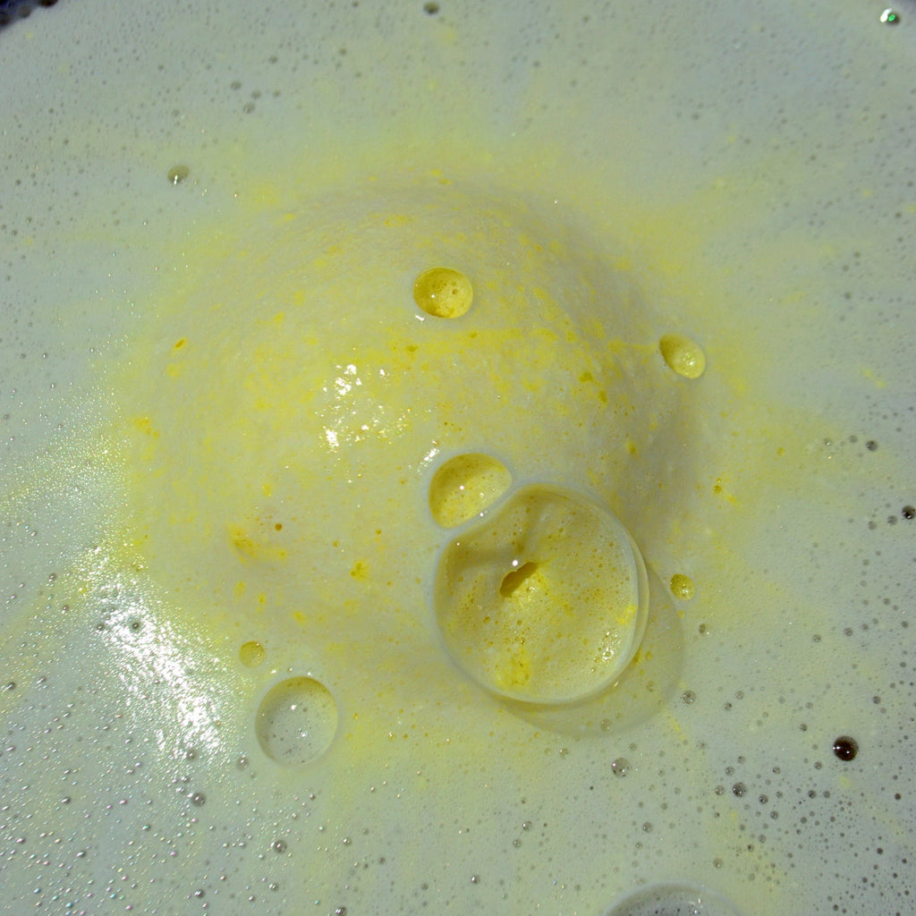 Yellow bath bomb with white and yellow foam surrounding it