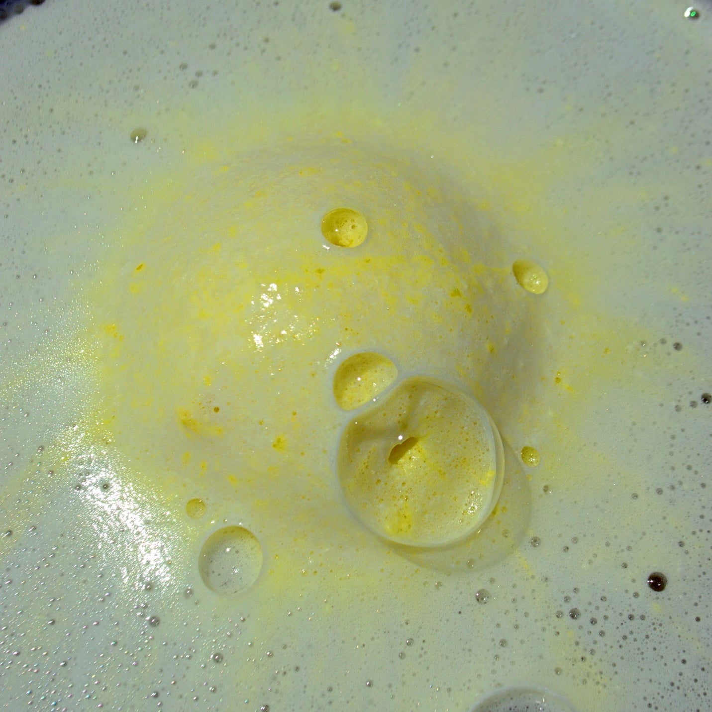 Yellow bath bomb with white and yellow foam surrounding it