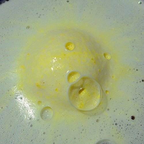 Yellow bath bomb with white and yellow foam surrounding it